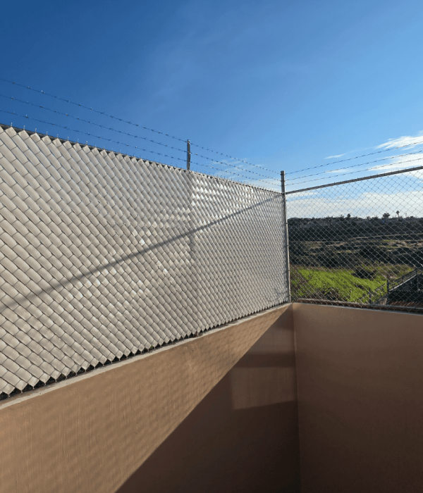 Cercado sobre barda con malla ciclónica galvanizada, cinta plástica de privacidad color beige o blanco y remate de alambre de púas en terraza o patio.